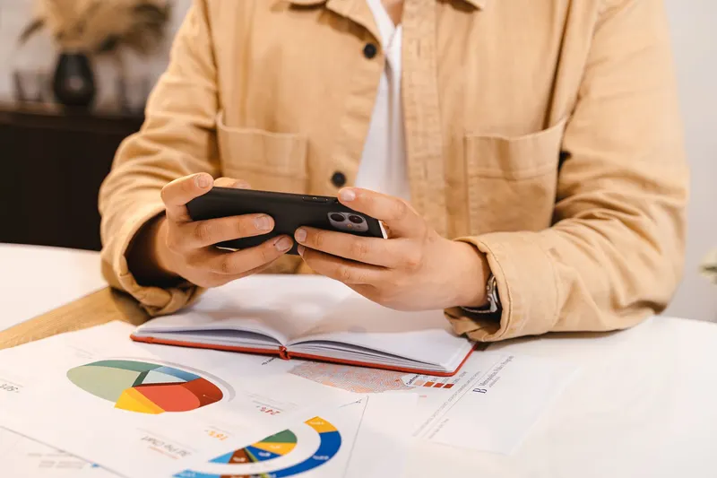 A person holding a phone over paper documents on a desk